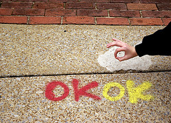 En rojo y amarillo aparece escrito OK en una baldosa y una mano haciendo el gesto