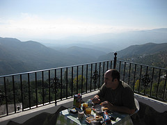 Hombre desayunando en una terraza con las montañas al fondo.